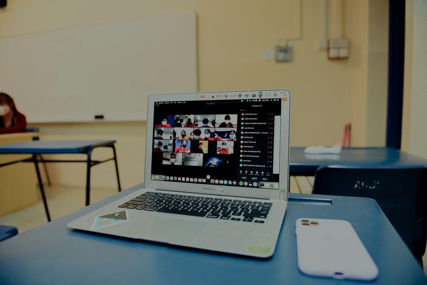 Un computer portatile mostra una videoconferenza su una scrivania blu da aula.